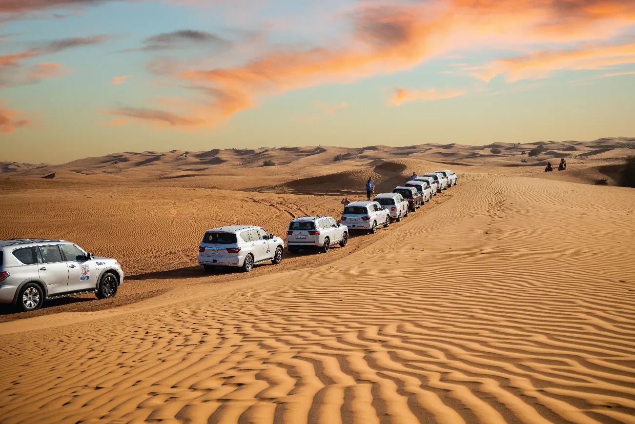 Desert safari convoy crossing the dunes at sunset