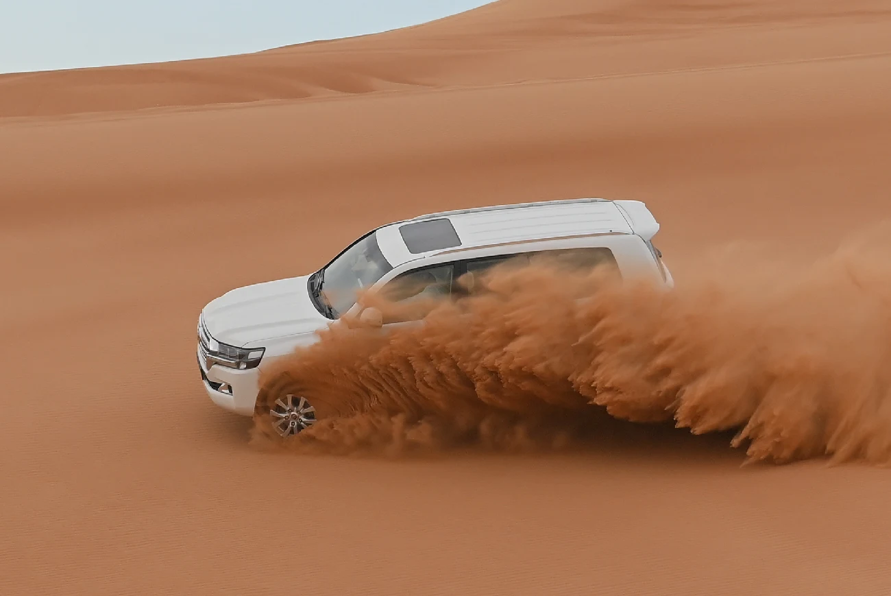 A white 4x4 driving across the desert dunes